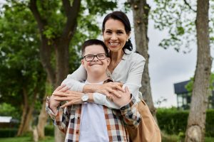 mother and her son with Down syndrome smiling outside surrounded by trees